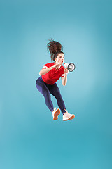 Image showing Beautiful young woman jumping with megaphone isolated over red background