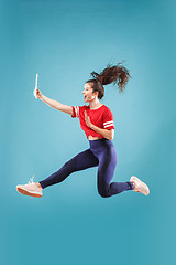 Image showing Image of young woman over pink background using laptop computer or tablet gadget while jumping.