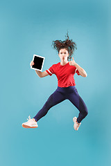 Image showing Image of young woman over pink background using laptop computer or tablet gadget while jumping.