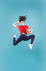 Image showing Forward to the victory.The young woman as soccer football player jumping and kicking the ball at studio on pink