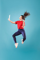 Image showing Image of young woman over pink background using laptop computer or tablet gadget while jumping.