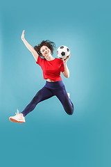 Image showing Forward to the victory.The young woman as soccer football player jumping and kicking the ball at studio on pink