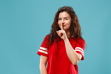 Image showing The young woman whispering a secret behind her hand over blue background