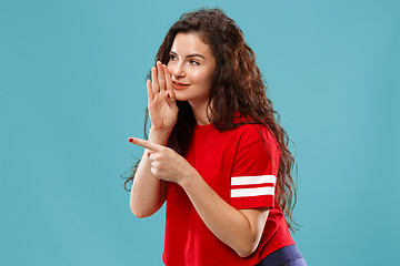 Image showing The young woman whispering a secret behind her hand over blue background