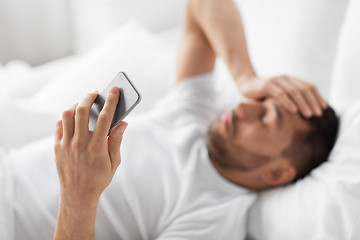 Image showing hand of young man with smartphone in bed