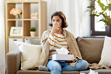 Image showing sick woman blowing nose in paper tissue at home