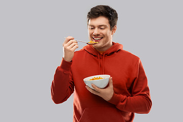 Image showing smiling young man in red hoodie eating cereals