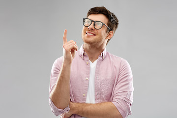 Image showing smiling young man in glasses pointing finger up