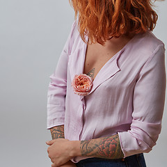 Image showing red-haired girl with fresh flower living coral color in hands with tattoo on a gray background. Gift on Woman\'s or Mother\'s Day.