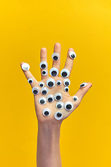 Image showing Girl\'s hand with plastic eyes on an yellow background.