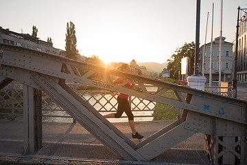 Image showing woman jogging across the bridge at sunny morning