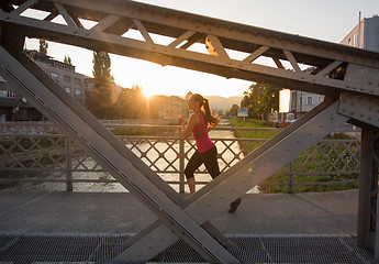 Image showing woman jogging across the bridge at sunny morning