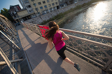 Image showing woman jogging across the bridge at sunny morning