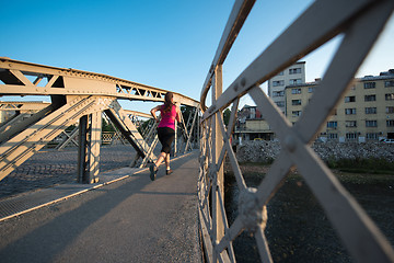 Image showing woman jogging across the bridge at sunny morning