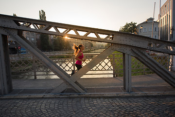 Image showing woman jogging across the bridge at sunny morning