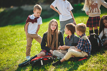 Image showing A group of children of school and preschool age are sitting on the green grass in the park.