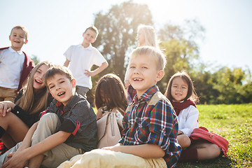 Image showing A group of children of school and preschool age are sitting on the green grass in the park.