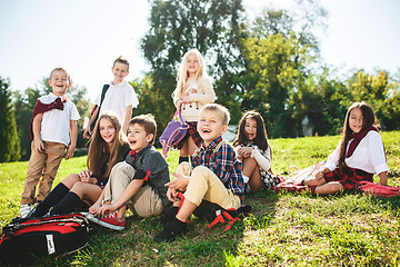 Image showing A group of children of school and preschool age are sitting on the green grass in the park.