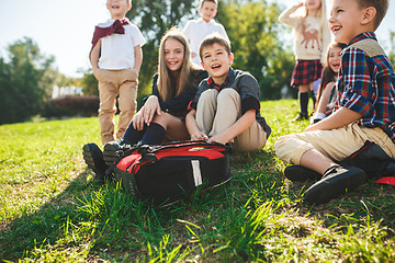 Image showing A group of children of school and preschool age are sitting on the green grass in the park.