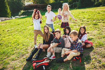 Image showing A group of children of school and preschool age are sitting on the green grass in the park.