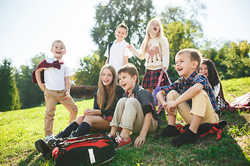 Image showing A group of children of school and preschool age are sitting on the green grass in the park.