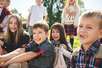 Image showing A group of children of school and preschool age are sitting on the green grass in the park.