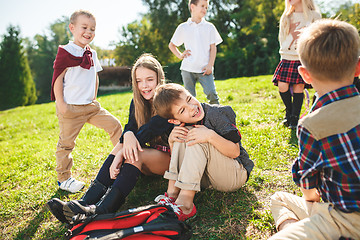 Image showing A group of children of school and preschool age are sitting on the green grass in the park.