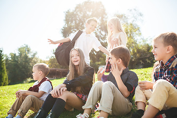 Image showing A group of children of school and preschool age are sitting on the green grass in the park.