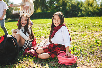 Image showing A group of children of school and preschool age are sitting on the green grass in the park.