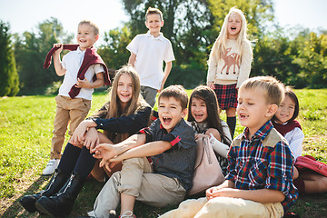 Image showing A group of children of school and preschool age are sitting on the green grass in the park.