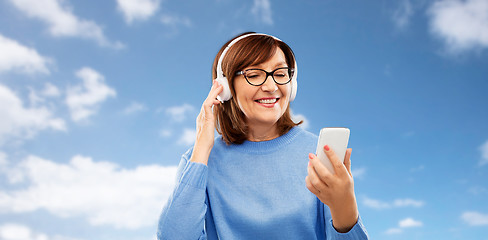 Image showing senior woman in headphones listening music on cell