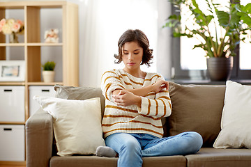 Image showing unhappy woman suffering from pain in hand at home