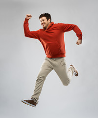 Image showing young man in hoodie jumping over grey background