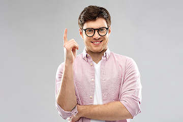 Image showing smiling young man in glasses pointing finger up