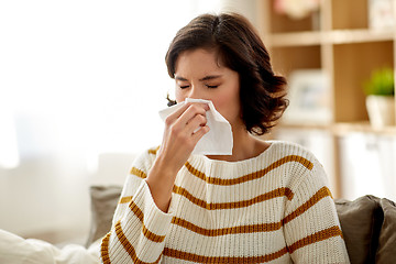 Image showing sick woman blowing nose in paper tissue at home