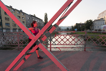 Image showing woman jogging across the bridge at sunny morning