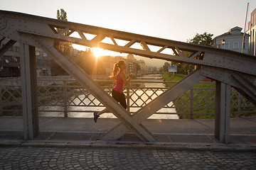 Image showing woman jogging across the bridge at sunny morning