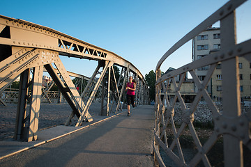 Image showing woman jogging across the bridge at sunny morning