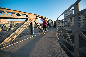 Image showing woman jogging across the bridge at sunny morning