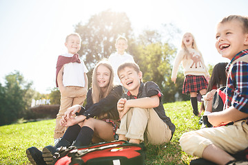 Image showing A group of children of school and preschool age are sitting on the green grass in the park.