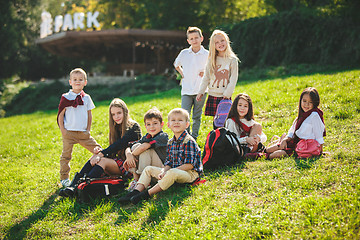 Image showing A group of children of school and preschool age are sitting on the green grass in the park.