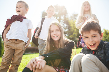 Image showing A group of children of school and preschool age are sitting on the green grass in the park.