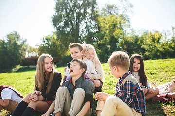 Image showing A group of children of school and preschool age are sitting on the green grass in the park.