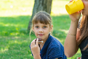 Image showing Girl eating a cupcake on a picnic, next to a girl drinking tea