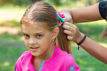 Image showing A teenager girl is tied a bow on long hair, on a picnic, close-up