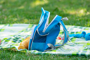 Image showing Children\'s backpack and bottle for water lie on a bedspread on a picnic