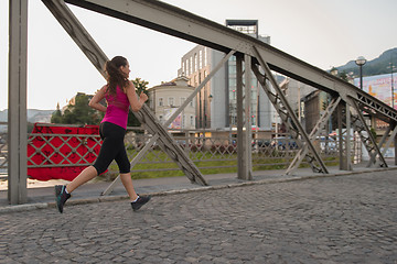 Image showing woman jogging across the bridge at sunny morning