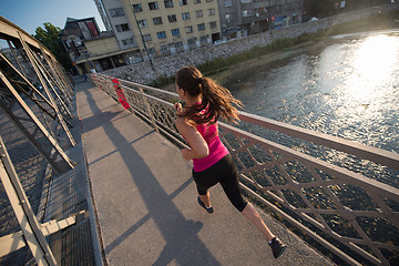 Image showing woman jogging across the bridge at sunny morning