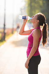 Image showing woman drinking water from a bottle after jogging