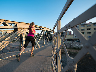 Image showing woman jogging across the bridge at sunny morning